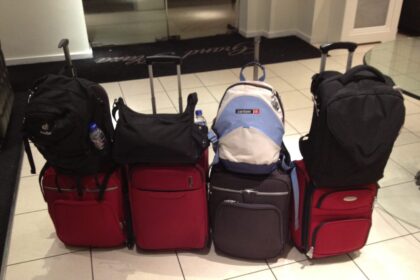Four backpacks or bags resting on wheeled suitcases in an archive luggage photograph
