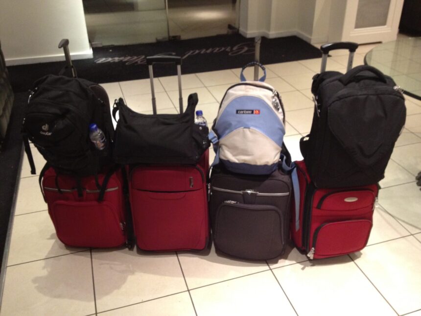 Four backpacks or bags resting on wheeled suitcases in an archive luggage photograph