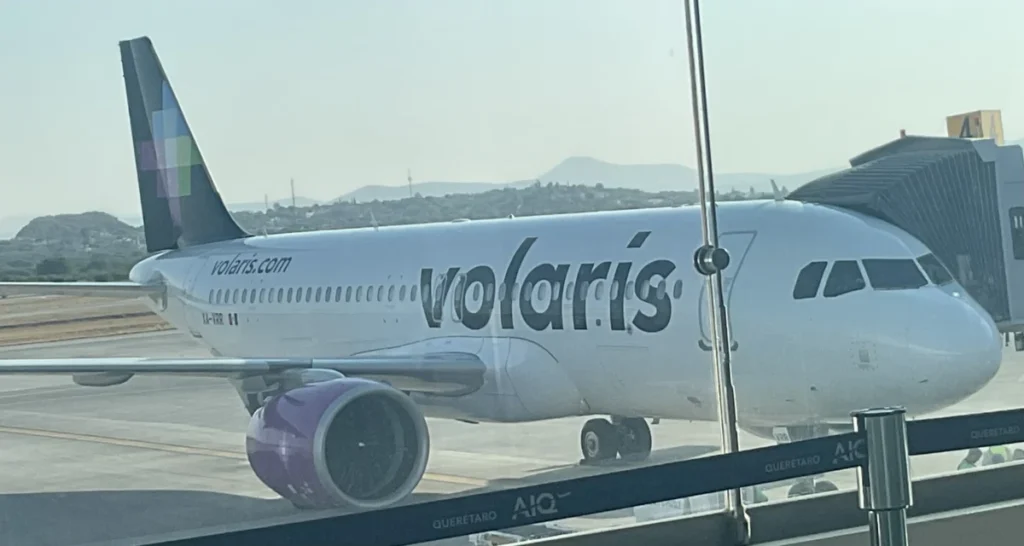 Archive Volaris Airbus A321neo parked at Querétaro airport in March 2024, seen through terminal glass.